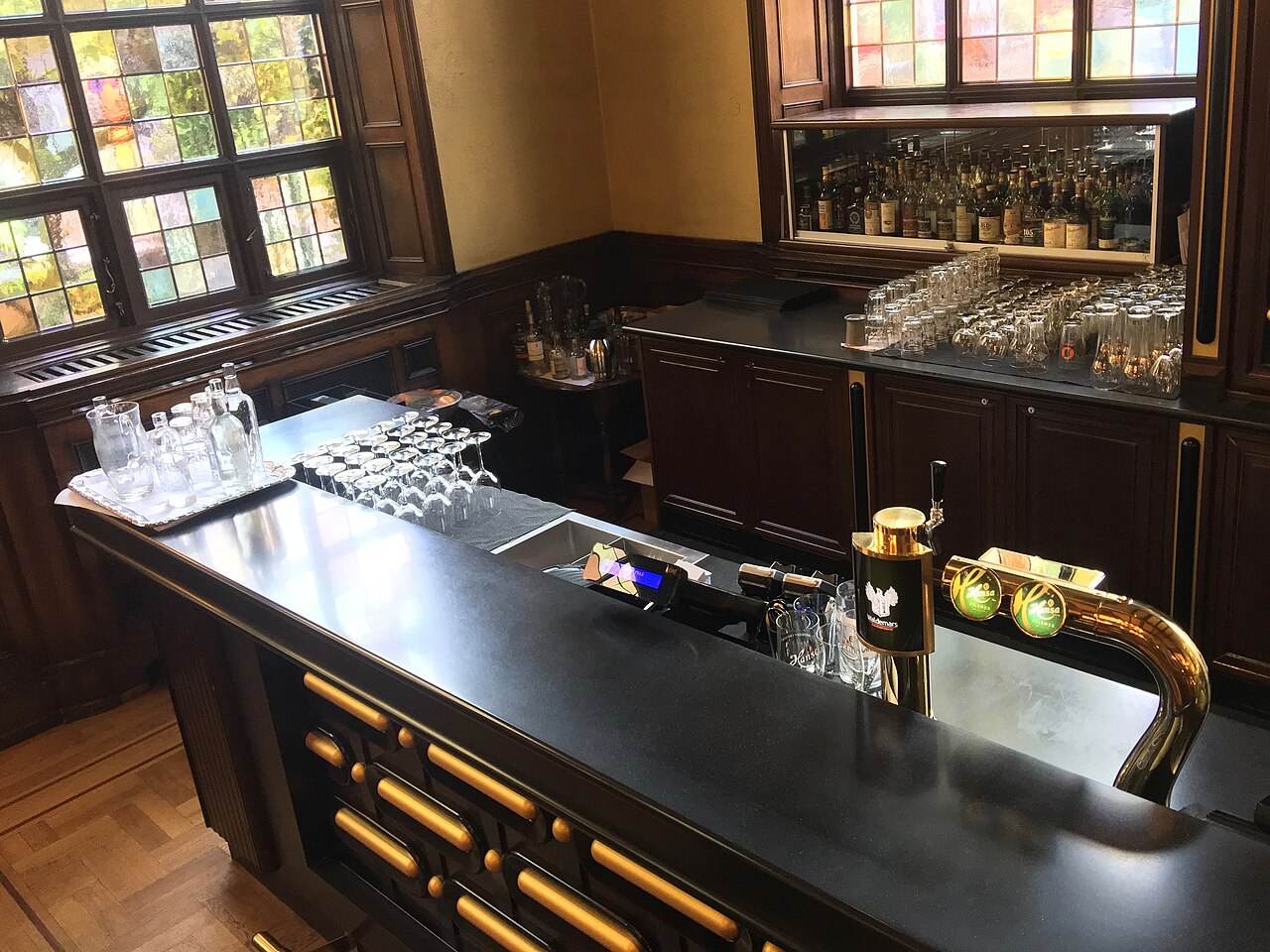 A dark wood bar counter with beer taps and glasses