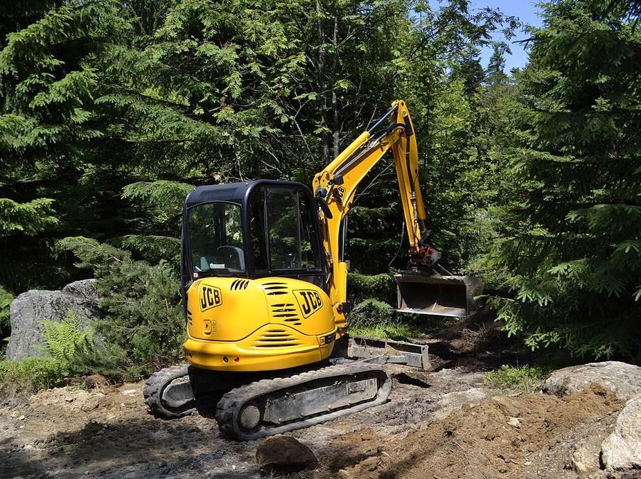 A yellow compact excavator digging on a work site