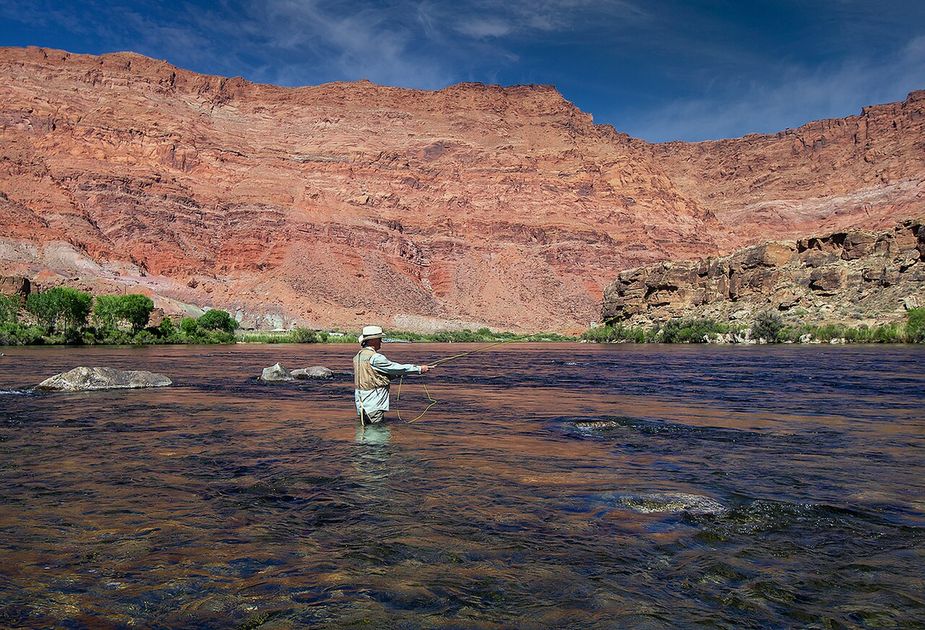 A fly fisher standing in a river below red cliffs