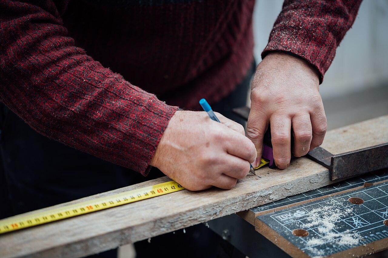 Hands marking a board with a pencil and tape measure