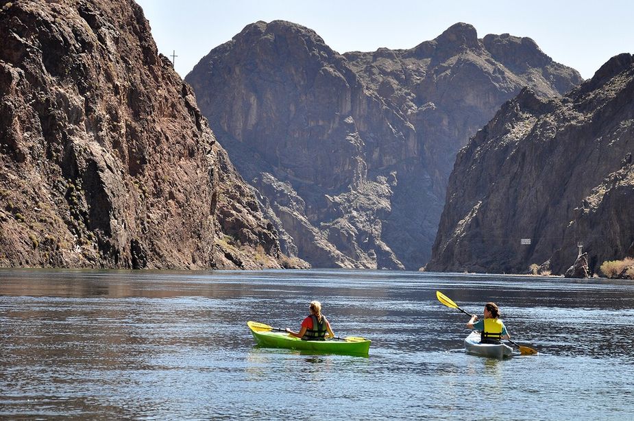 Two kayakers paddling through a desert canyon