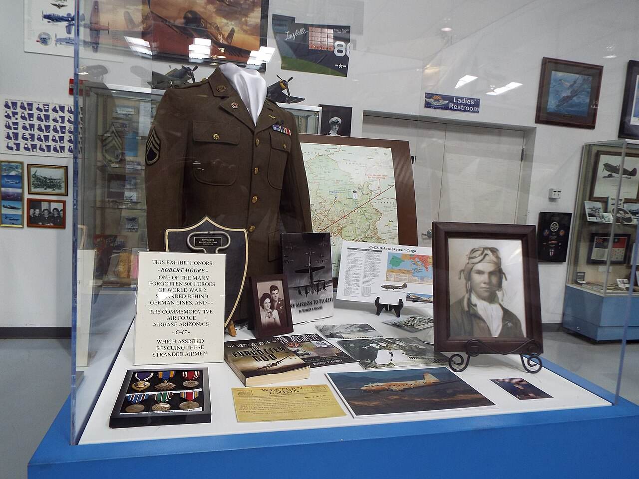 A museum display case with a uniform, photos and papers