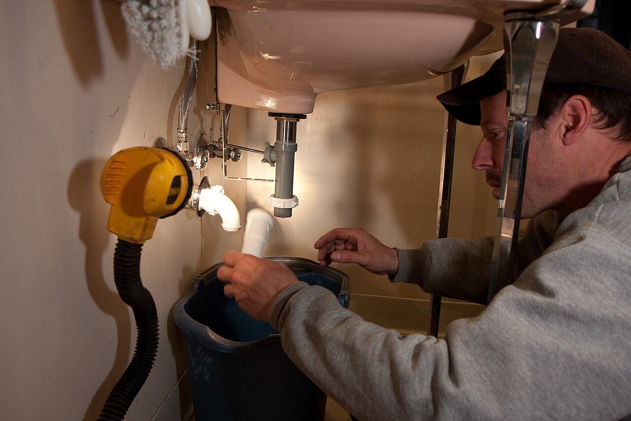 A plumber working on the drain under a kitchen sink