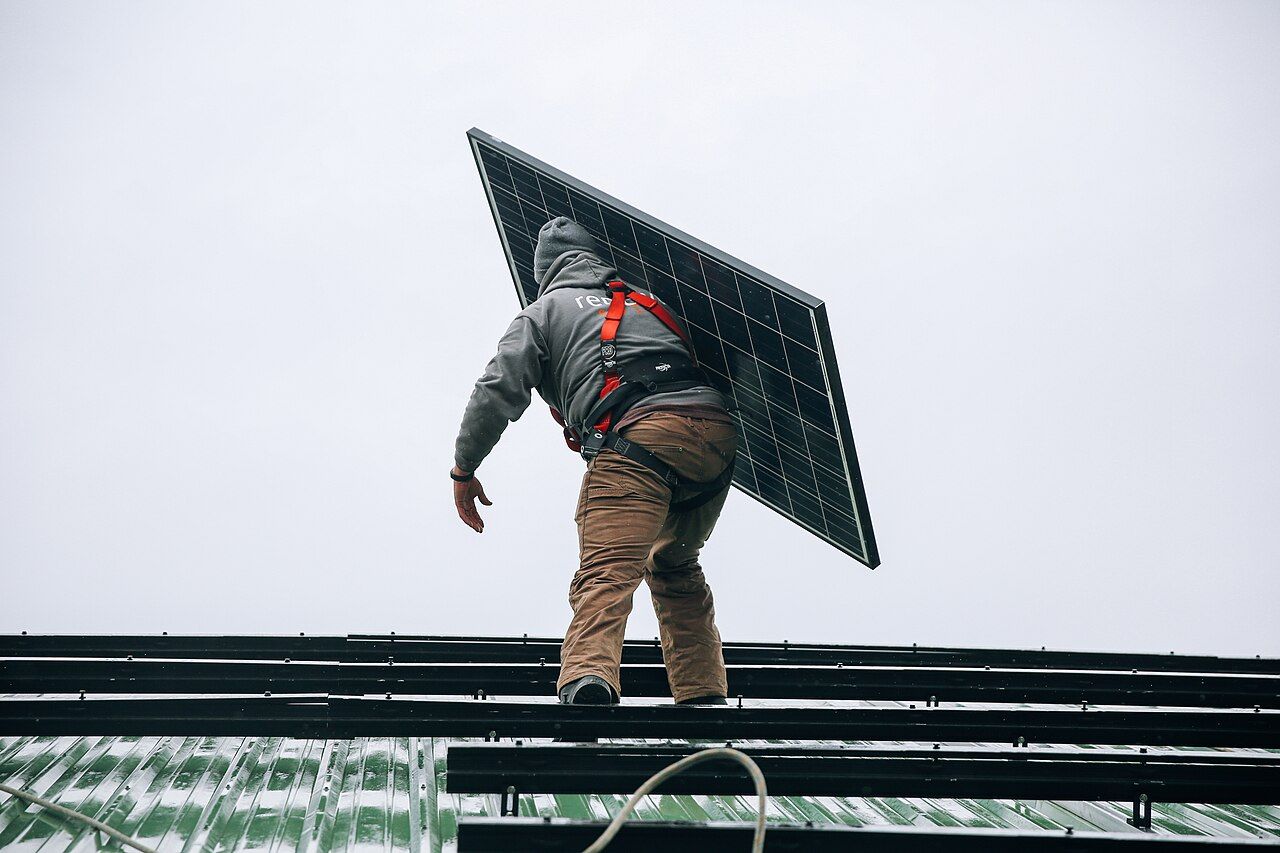 A technician carrying a solar panel across a roof