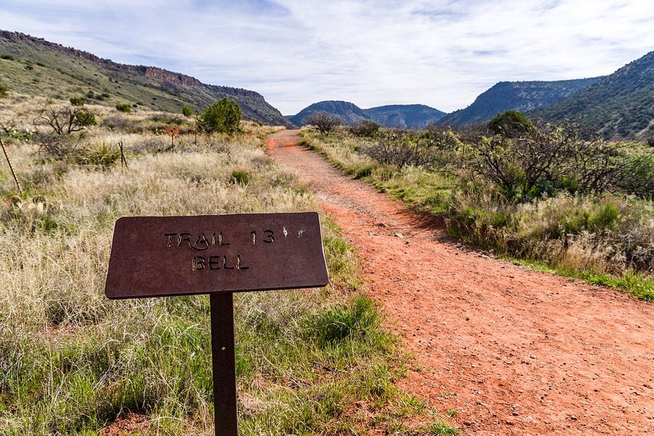 A red dirt hiking trail through grass toward the hills
