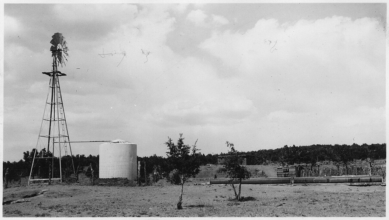 A windmill water well with a storage tank, in black and white
